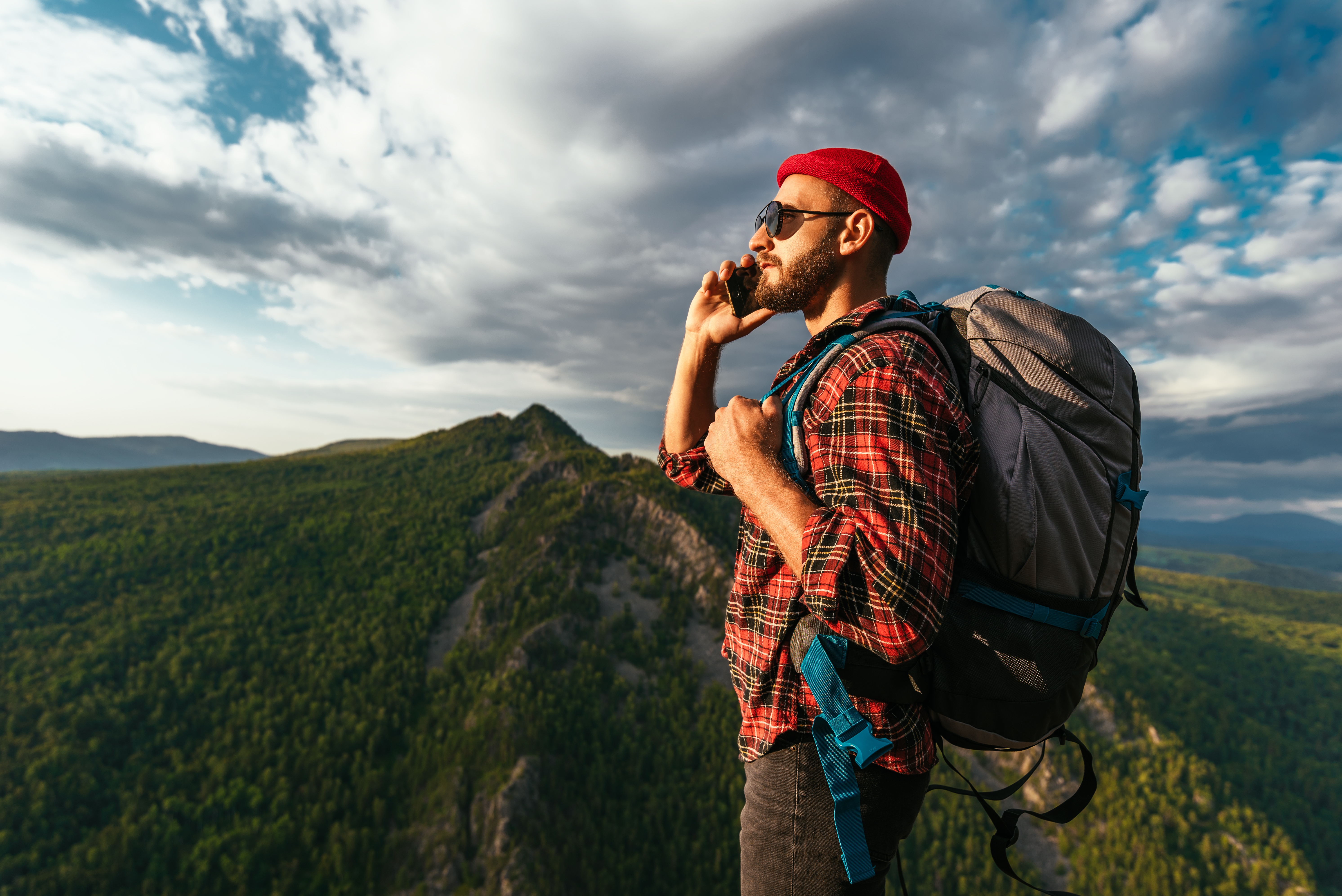 A man in hiking clothes talks on a smartphone at sunset in the mountains. Phone conversation